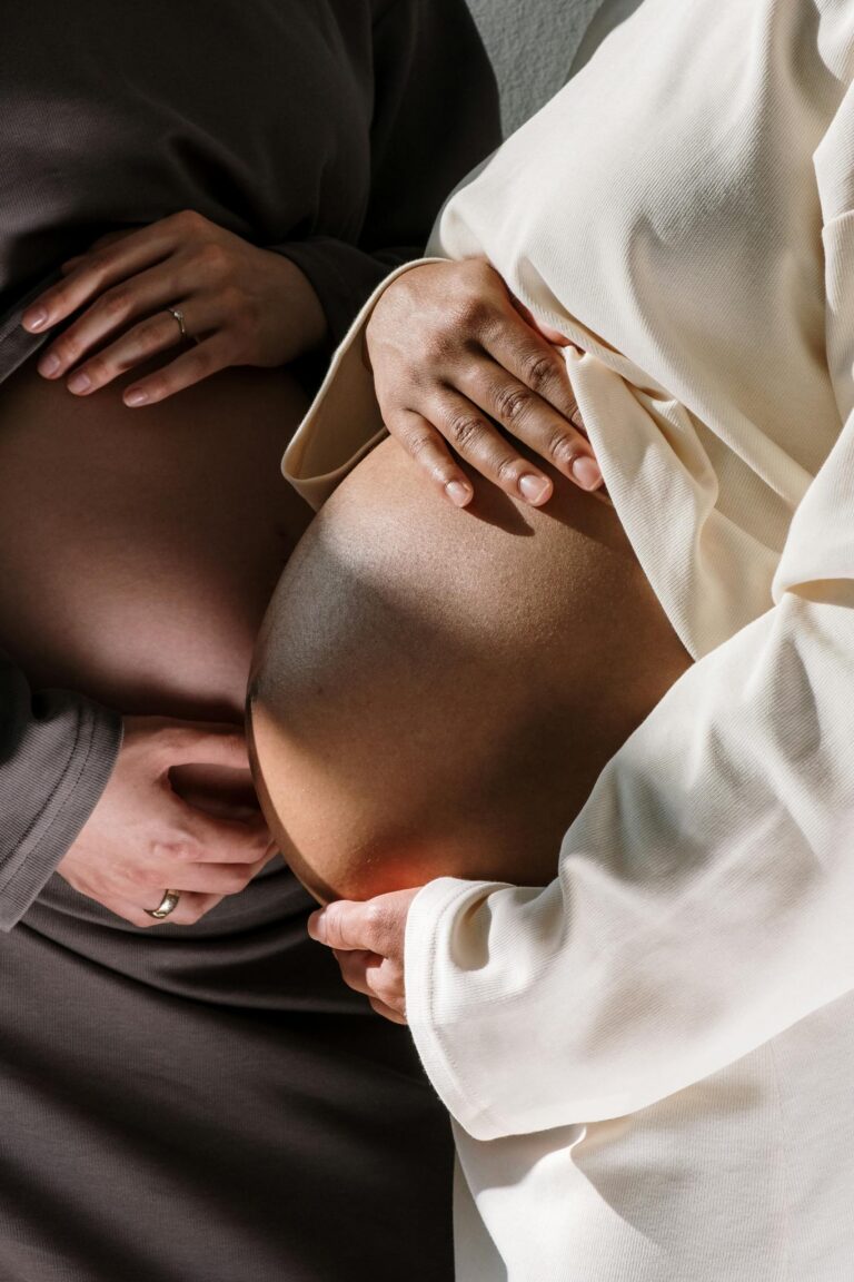 A close-up view showing two pregnant women embracing their baby bumps.